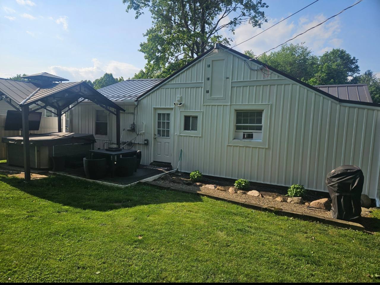 White house rear exterior with covered hot tub pavilion, outdoor TV, seating and lawn