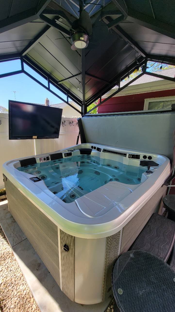 Private hot tub beneath a covered pavilion with ceiling fan and outdoor television