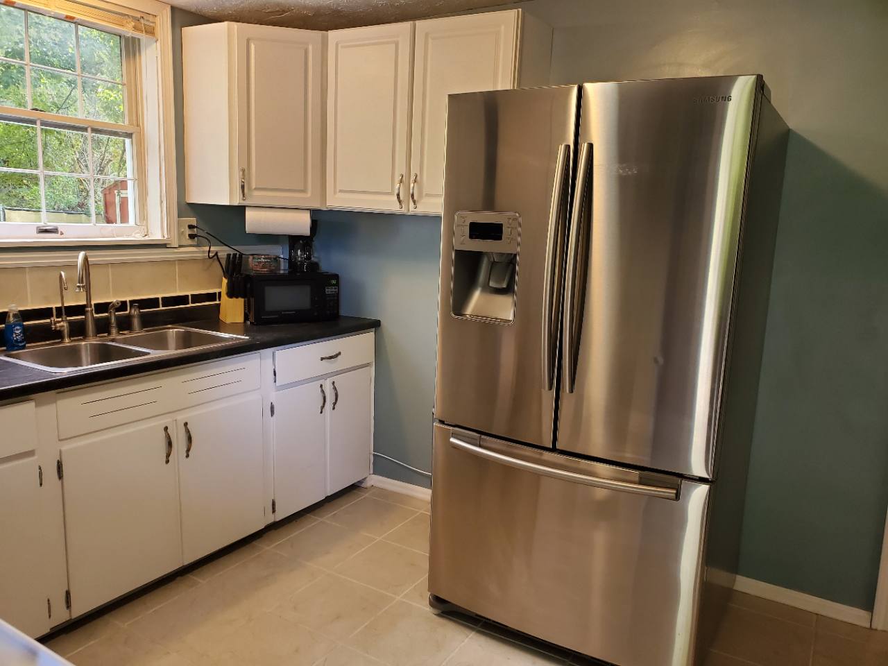 Kitchen with white cabinets, stainless steel refrigerator, double sink, microwave and coffee maker