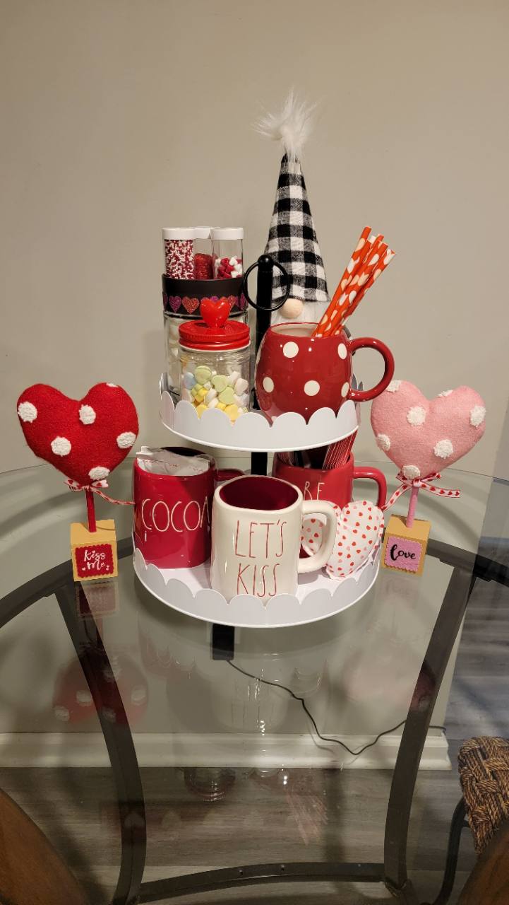 Seasonal heart decorations, red and white mugs and cocoa toppings on a glass table