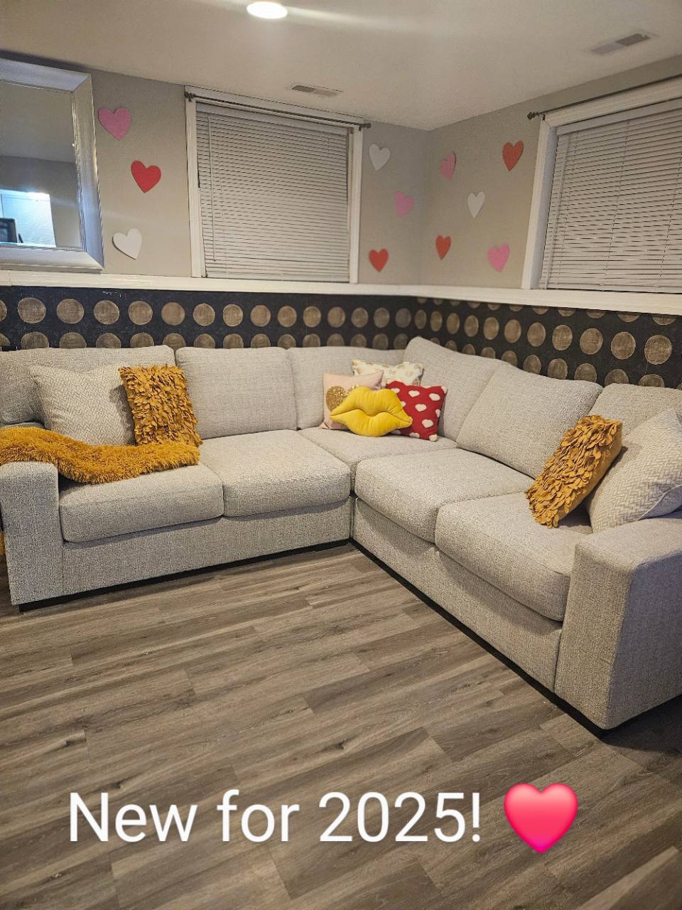 Gray sectional sofa with yellow pillows and seasonal heart decorations, with New for 2025 text on the photo